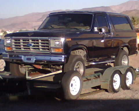 1985 Ford Bronco - A black 1985 Ford Bronco is seen loaded onto a trailer, viewed from the front three-quarter angle.