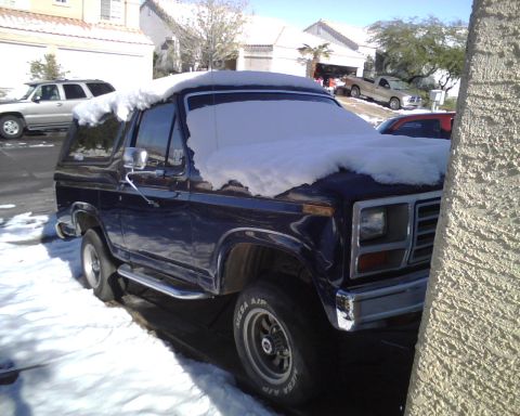 1985 Ford Bronco - Dark blue 1985 Ford Bronco with snow on its roof and windshield, parked outside.