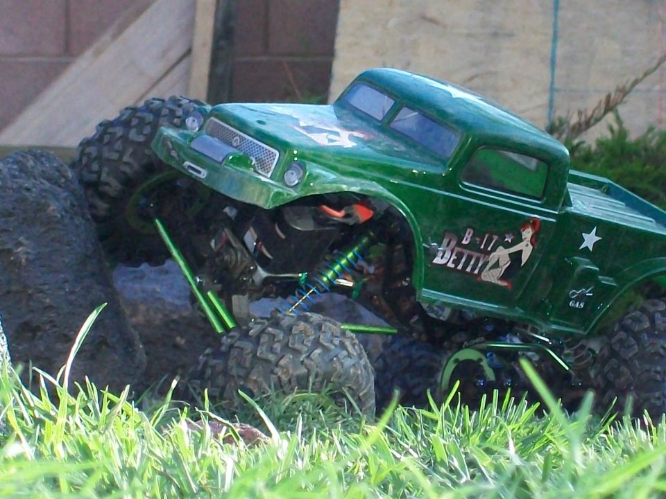 Green remote control monster truck with 'B-17 Betty' decal climbing over rocks and grass
