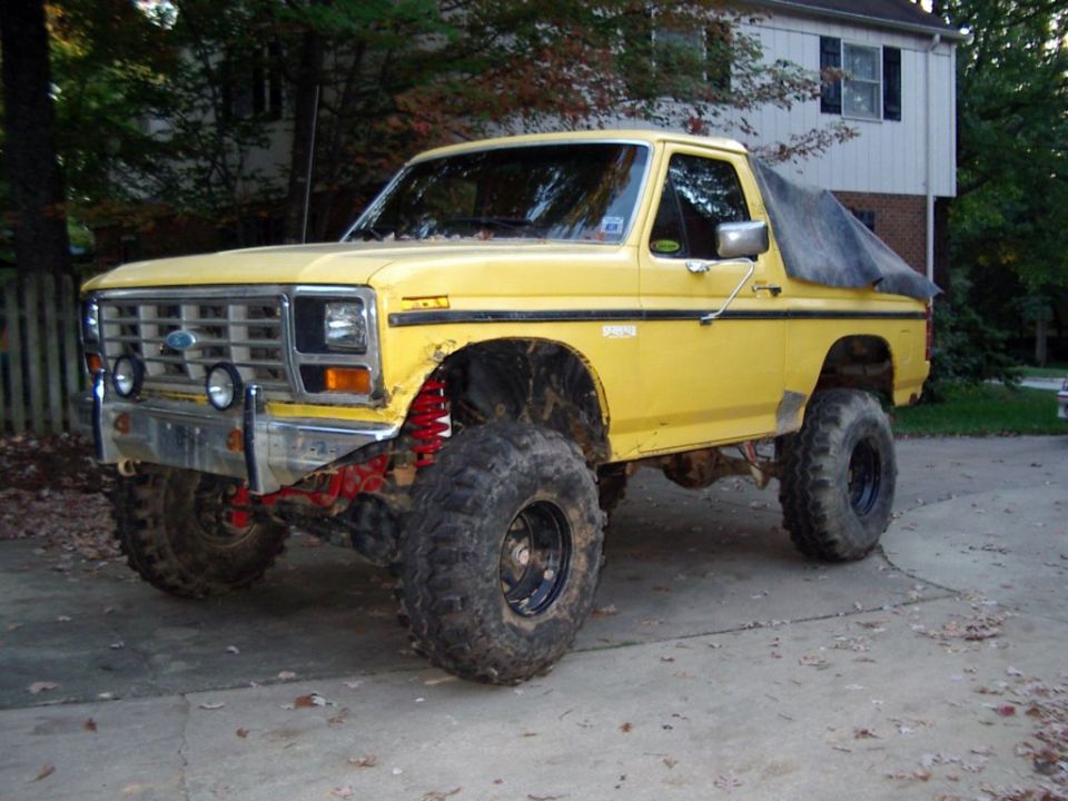 Yellow lifted Ford Bronco with top down on large mud tires in a driveway