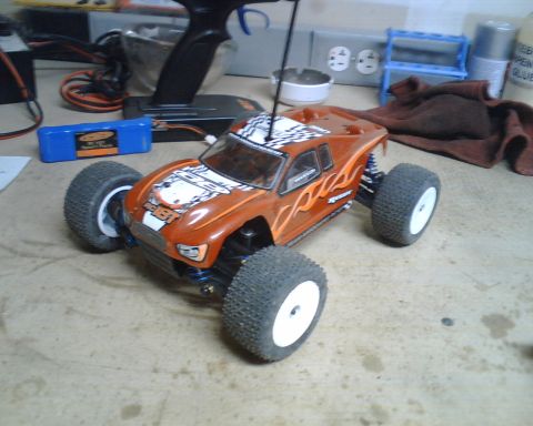 1985 Ford Bronco - A remote control truck sits on a workbench next to a battery and controller.