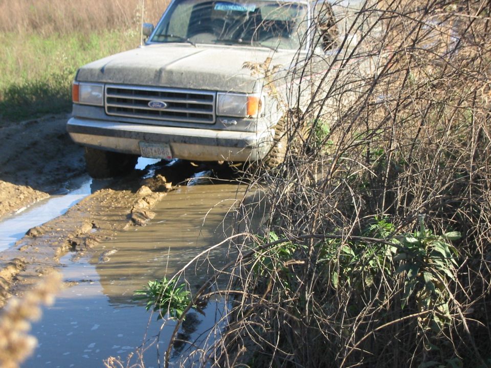 1991 Ford Bronco driving through a muddy trail, front end visible