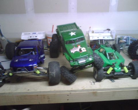 1985 Ford Bronco - Several remote control monster trucks are lined up on a wooden surface.
