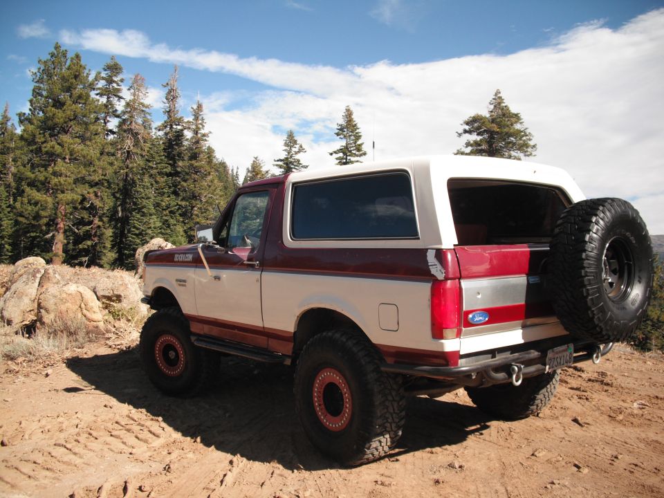 Two-tone maroon and white Ford Bronco with a spare tire mounted on the rear, parked on a dirt road