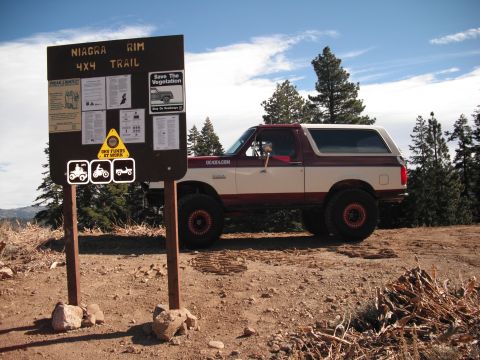 1991 Ford Bronco - A two-tone red and white Ford Bronco is parked next to the Niagra Rim 4x4 Trail sign in a wooded, mountainous area.