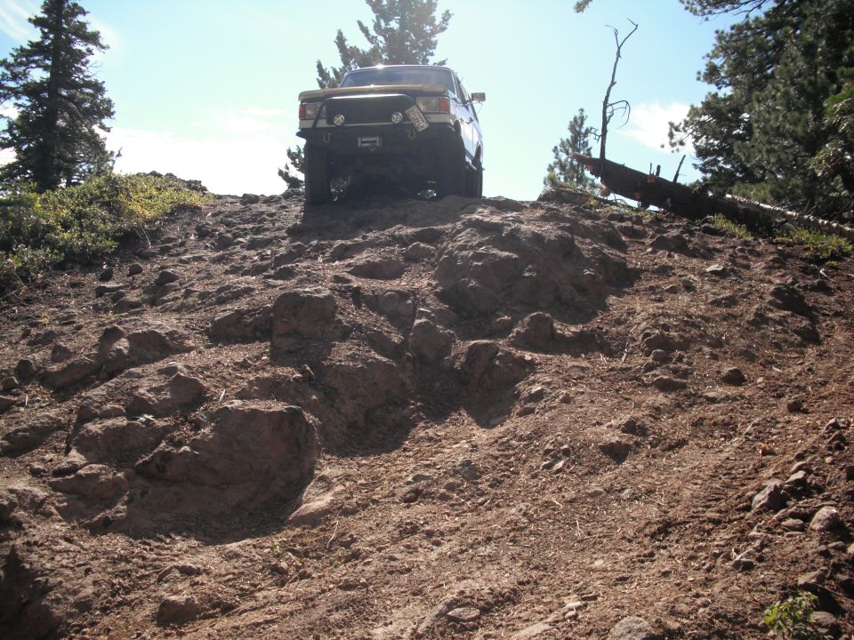 Yellow off-road vehicle climbing a steep, rocky hill with trees in the background