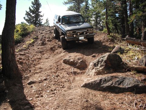 1991 Ford Bronco - This Chevrolet K5 Blazer is navigating a challenging, rocky trail surrounded by trees.
