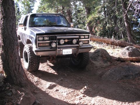 1991 Ford Bronco - This lifted black SUV navigates a challenging off-road trail, displaying an "UNDER CONSTRUCTION 4X4" sticker on its windshield.