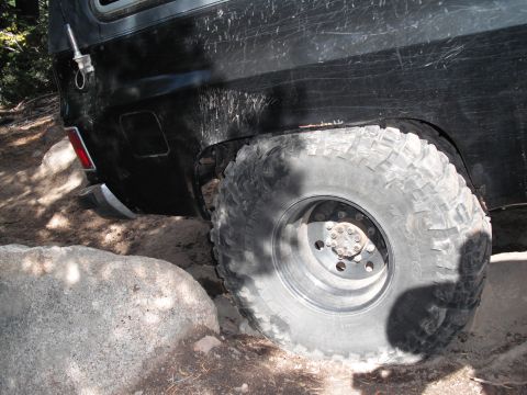 1991 Ford Bronco - The rear wheel of a black SUV is shown close-up as it traverses a challenging, rocky path.