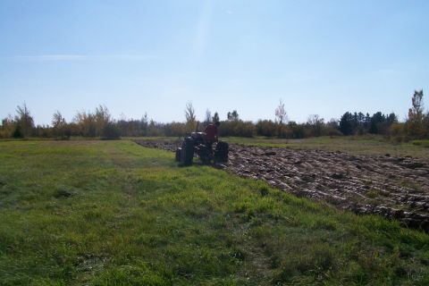 2000 Chevrolet Tahoe - A tractor is seen plowing a field under a clear blue sky.