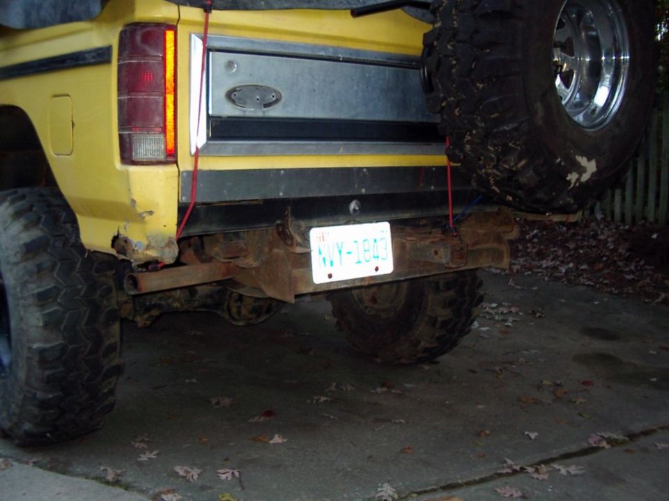 Rear of yellow Ford Bronco with big spare mud tire strapped to tailgate, plate NVY-1843, rusty bumper
