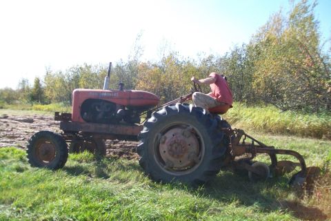 2000 Chevrolet Tahoe - A person operates a red tractor with a plow attachment in a field.