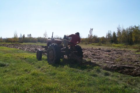 2000 Chevrolet Tahoe - A person operates a tractor, plowing a field under a clear blue sky.