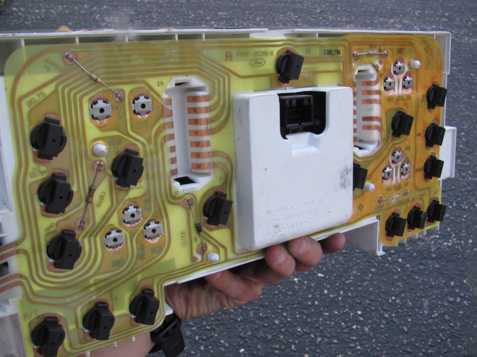 Back of a Ford instrument cluster showing yellow flex circuit and bulb sockets