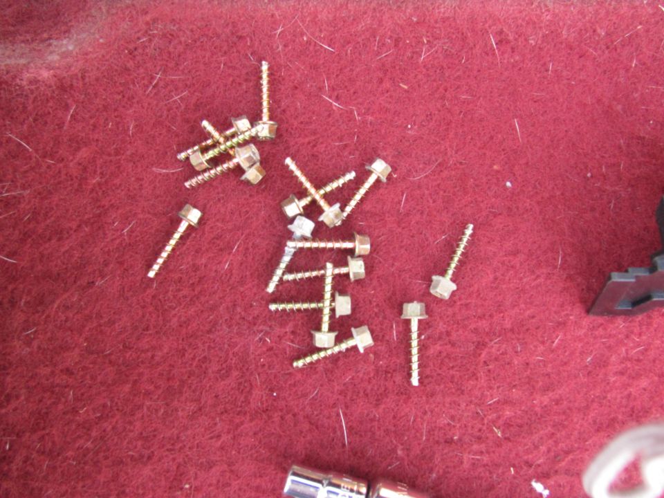 Gold zinc hex-head self-tapping screws scattered on red automotive carpet