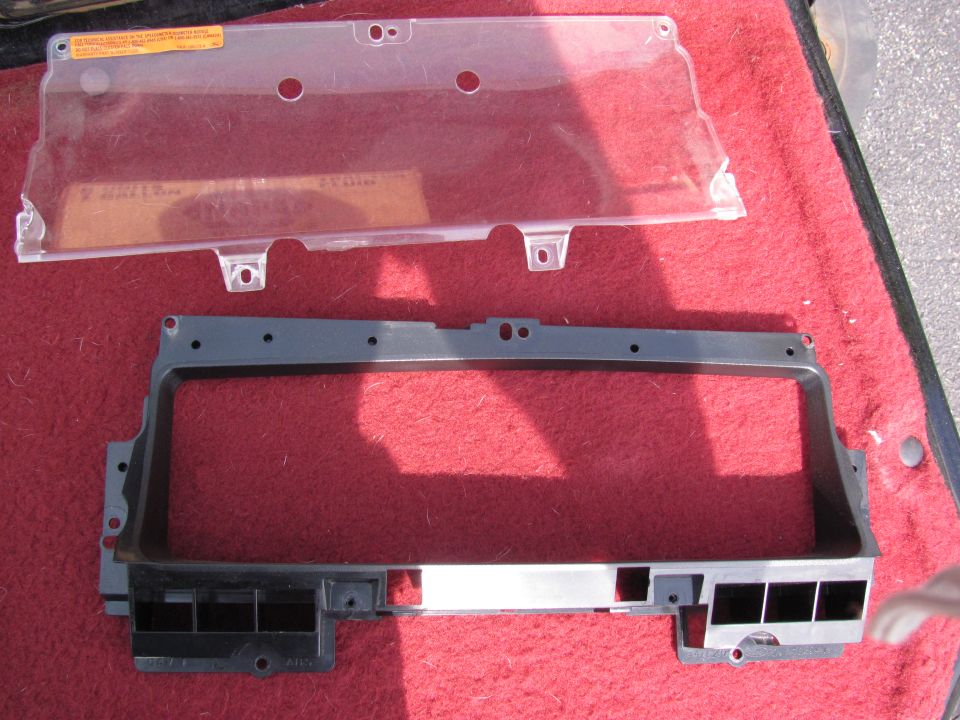 Clear instrument cluster lens and gray dash bezel laid out on red carpet