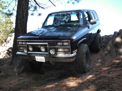 1991 Ford Bronco - This black SUV is equipped with large off-road tires and a brush guard, navigating a rocky trail.