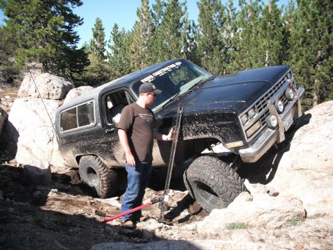 1991 Ford Bronco - A man uses a hi-lift jack to free a black off-road SUV that is stuck on large rocks.