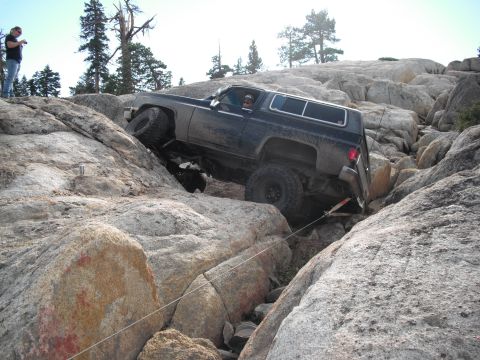 1991 Ford Bronco - A dark-colored SUV navigates a rocky terrain, appearing to be from the 1973 model year.