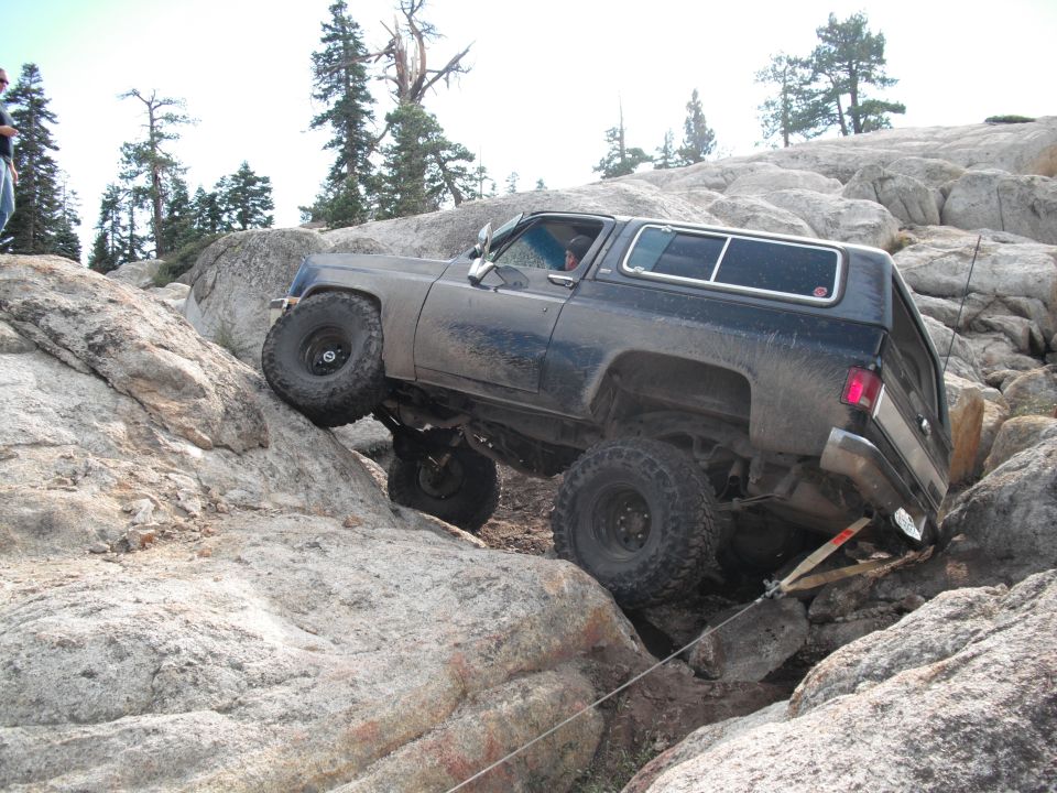 Dark blue off-road SUV with large tires climbing over large rocks on a trail