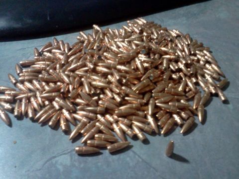 1996 Ford Bronco - A large quantity of copper-jacketed bullets are piled on a flat surface, with a website logo visible in the lower right corner.