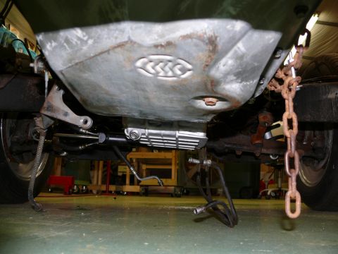 1976 Chevrolet Corvette - The underside of a vehicle is shown, with focus on the oil pan and suspension parts, and a rusty chain attached.