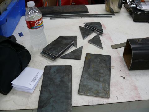 1976 Chevrolet Corvette - Various metal pieces, including rectangular plates and triangular shapes, are arranged on a table alongside a bottle of water and some pape…
