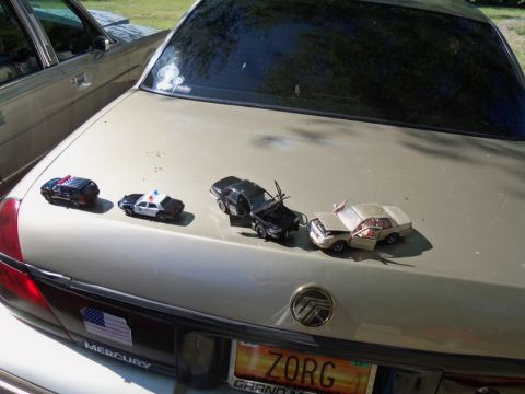 2000 Mercury Grand Marquis - A 2000 Mercury Grand Marquis displays toy police cars and a damaged toy car on its trunk.