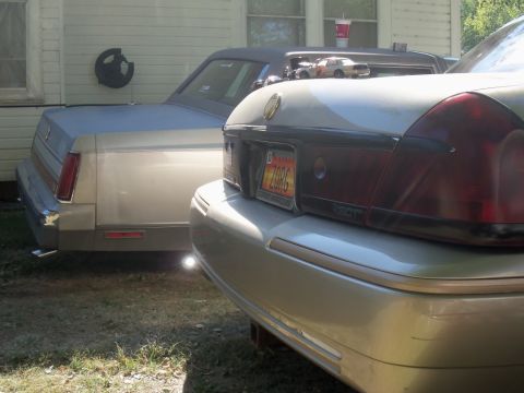 2000 Mercury Grand Marquis - Two sedans are parked next to each other in a yard. One is a 2000 Mercury Grand Marquis.