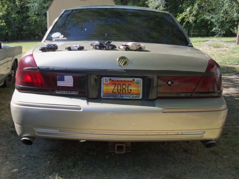 2000 Mercury Grand Marquis - Rear view of a gold Mercury Grand Marquis with a Kansas license plate and toy cars on the trunk.