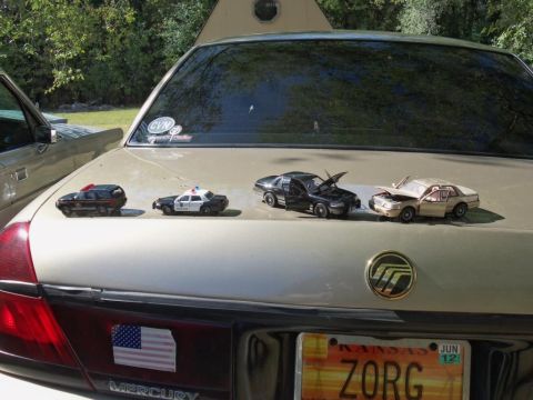 2000 Mercury Grand Marquis - A collection of toy cars, including police vehicles, are displayed on the trunk of a gold Mercury Grand Marquis.