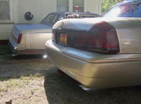 2000 Mercury Grand Marquis - Two sedans are parked in a grassy area next to a building. One has a license plate from 2006.