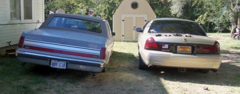 2000 Mercury Grand Marquis - Two sedans parked in a yard, one is a cream-colored Mercury Grand Marquis.