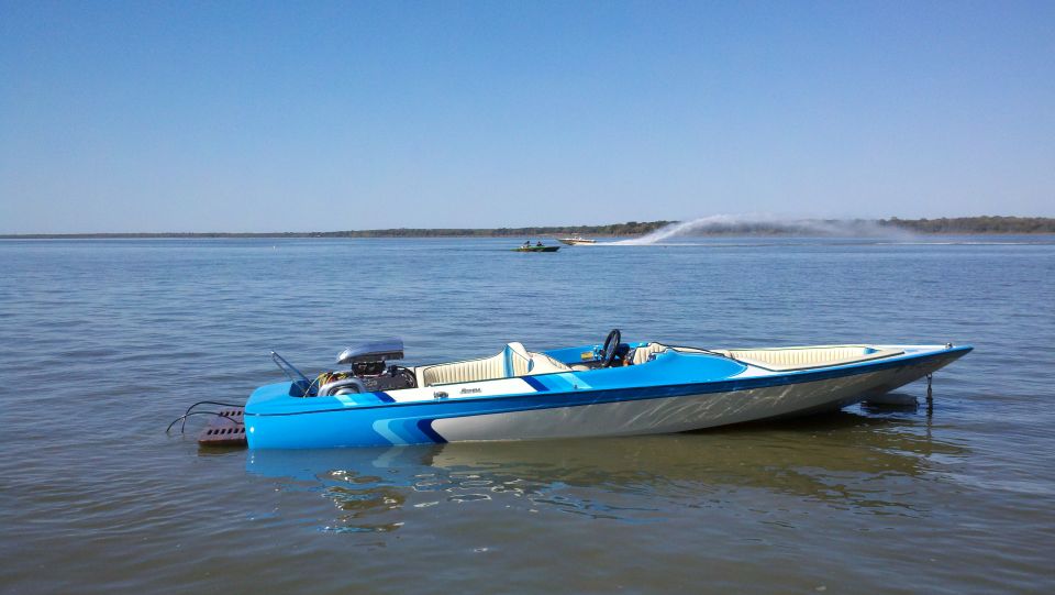 Blue and white speed boat with exposed engine, moored on calm water