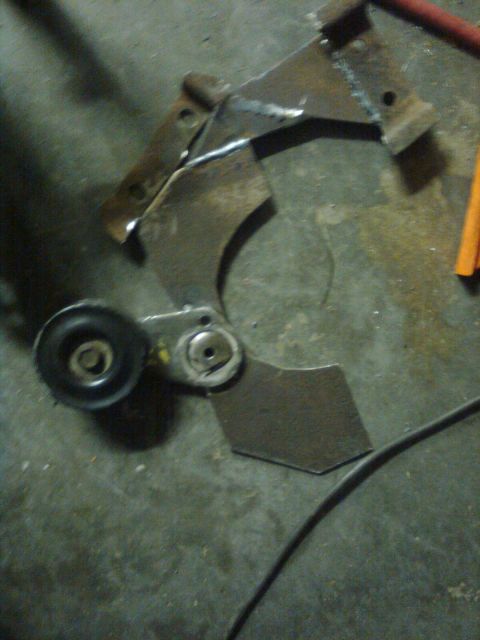 1984 Ford Bronco - A close-up view of a metal bracket with a pulley attached, likely a vehicle part.
