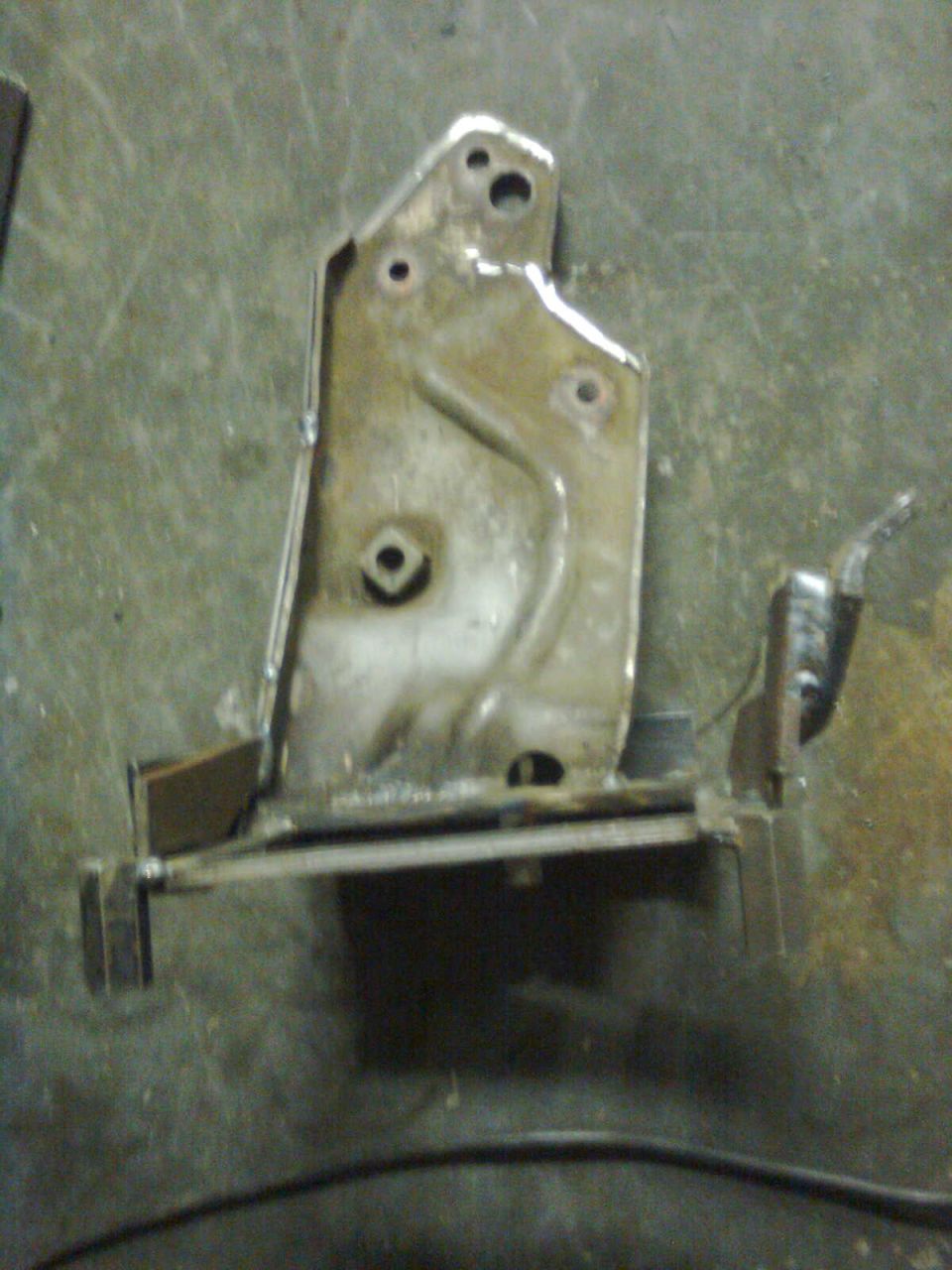 Metal bracket with welded extensions and mounting holes on a workshop floor