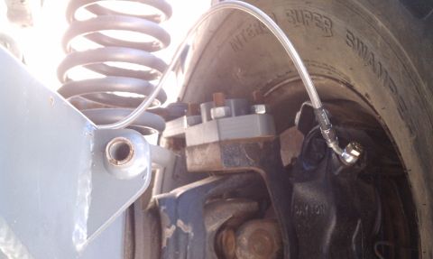 1979 Ford Bronco - Detail of a vehicle's brake system, including a caliper, spring, and brake line, with visible tire markings.
