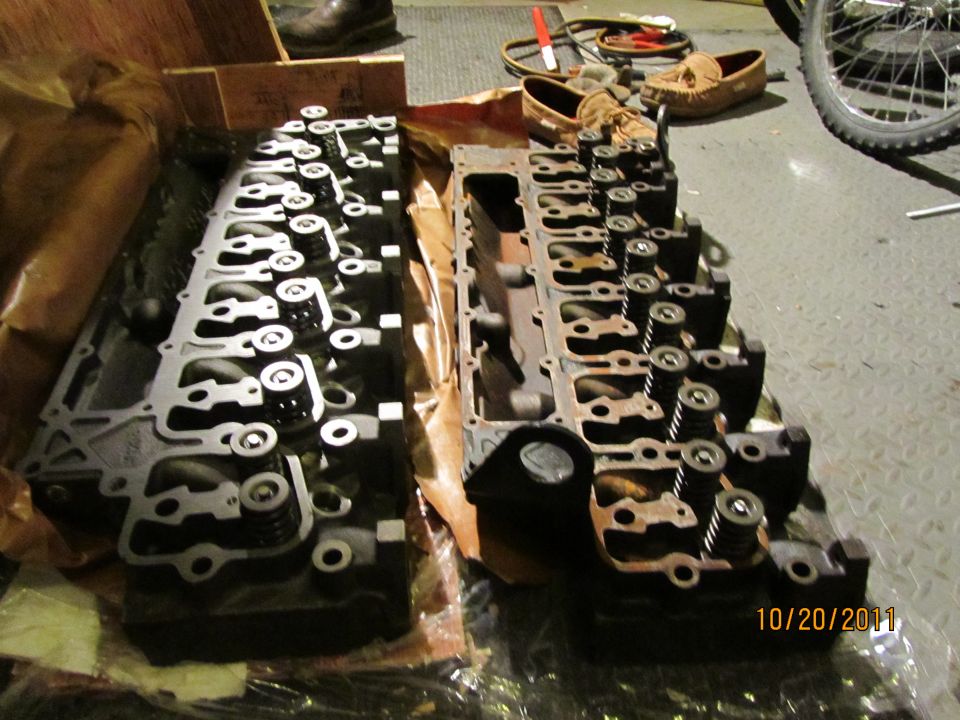 Two engine cylinder heads are laid out on a floor, one on the left and one on the right. A date stamp reads 10/20/2011