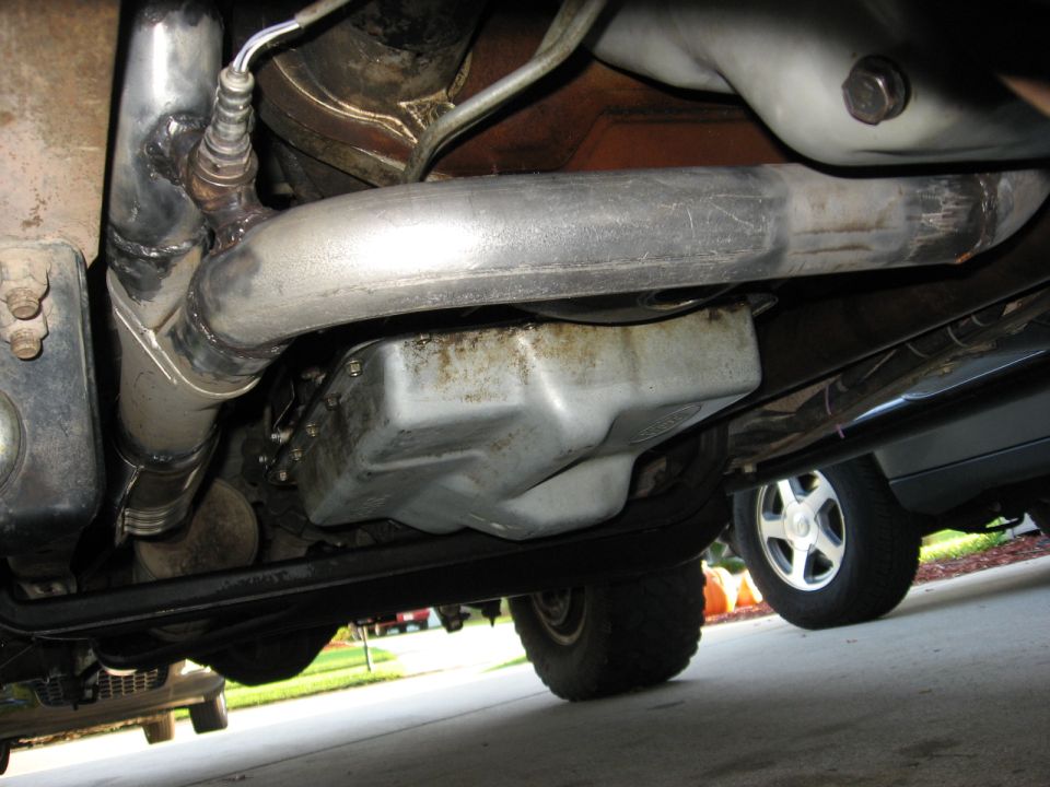 Underside of a vehicle showing exhaust pipe, oil pan, and a rear tire of another vehicle