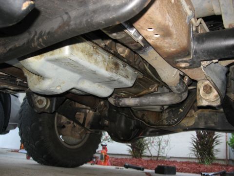 1994 Ford Bronco - The underside of a vehicle, focusing on the transmission pan and exhaust pipes, with a tire visible.