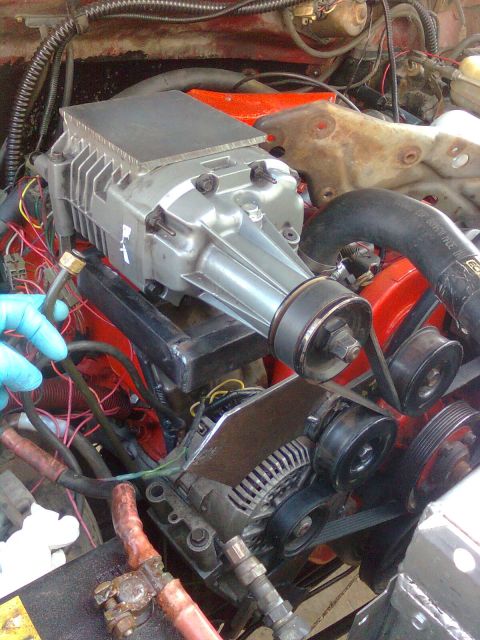 1984 Ford Bronco - Close-up view of an engine bay a prominent silver supercharger installed on a red engine block.