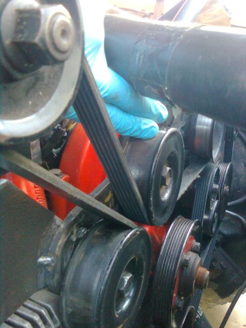 1984 Ford Bronco - Close-up view of a vehicle's engine belt system with a hand adjusting a belt on the pulleys.
