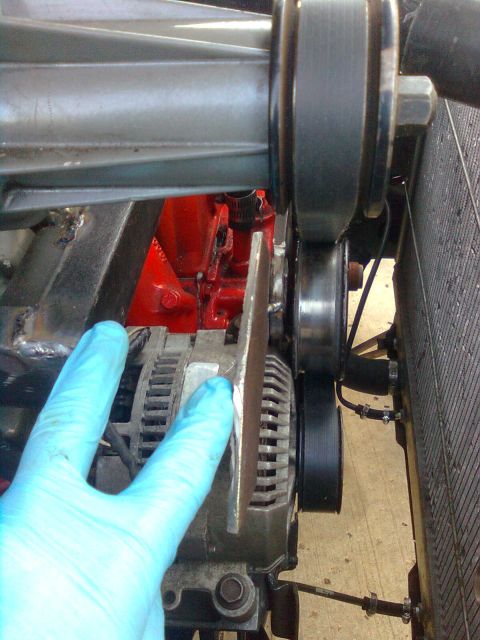 1984 Ford Bronco - Close-up view of engine components, including an alternator and radiator, with gloved hands making adjustments.