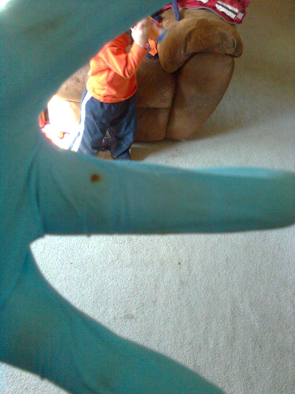 Child in orange sweatshirt and blue pants plays with a toy near a large brown recliner