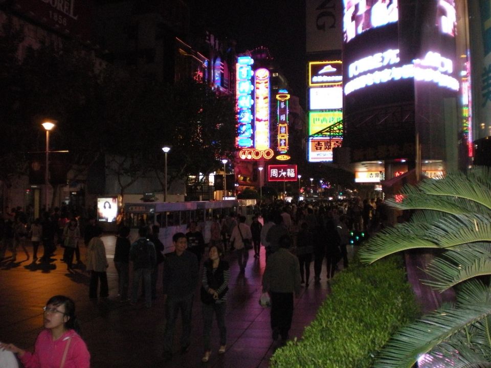 Crowded nighttime shopping street with neon signs and pedestrians