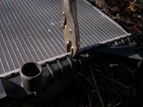 1997 Ford Taurus - A close-up view shows a pair of pliers being used on the edge of a vehicle's radiator.