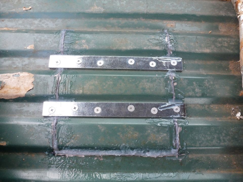 Two metal plates secured with screws over a seam on green corrugated metal