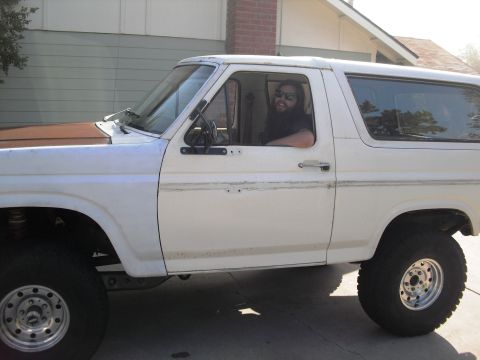 1986 Ford Bronco - Man sits in the driver's seat of a 1986 Ford Bronco parked in a driveway.