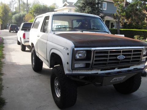 1986 Ford Bronco - A lifted white Ford Bronco is parked on a residential street, followed by a pickup truck and an SUV.