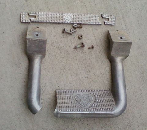 1996 Ford Bronco - Two aluminum step bars and a separate mounting bracket, along with screws and nuts, lie on a concrete surface.